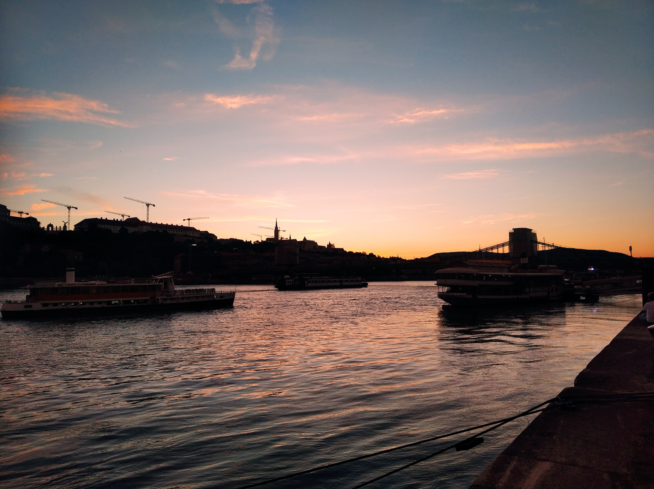 Sunset over the Danube in Budapest, with boats silhouetted against an orange sky and the Buda hills in the distance