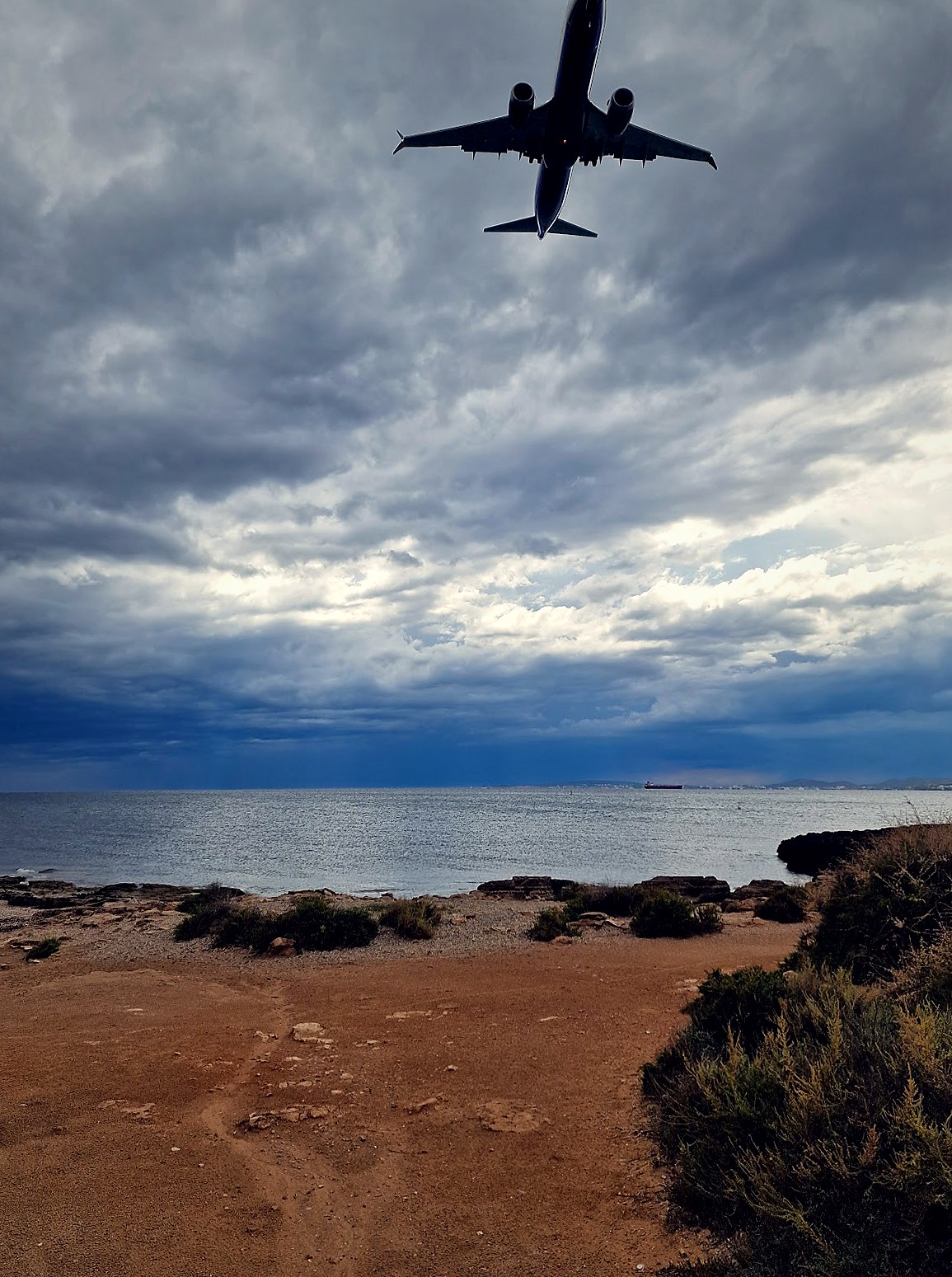 A commercial airliner descending low over the rocky coast near Ca'n Pastilla on approach to Palma airport