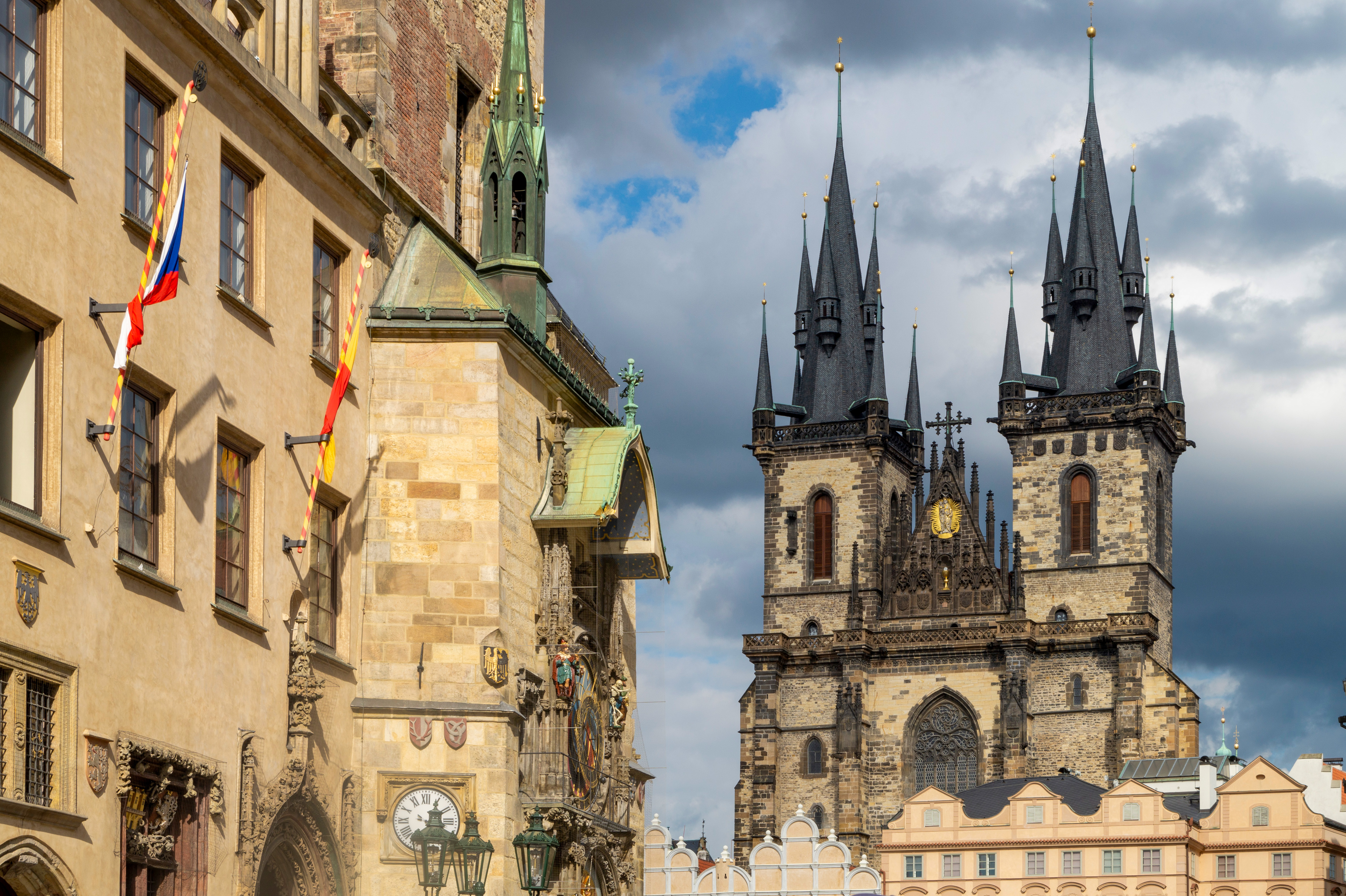 Corner of Prague's Old Town Hall with the Astronomical Clock and the twin Gothic towers of Týn Church behind it under a dramatic sky