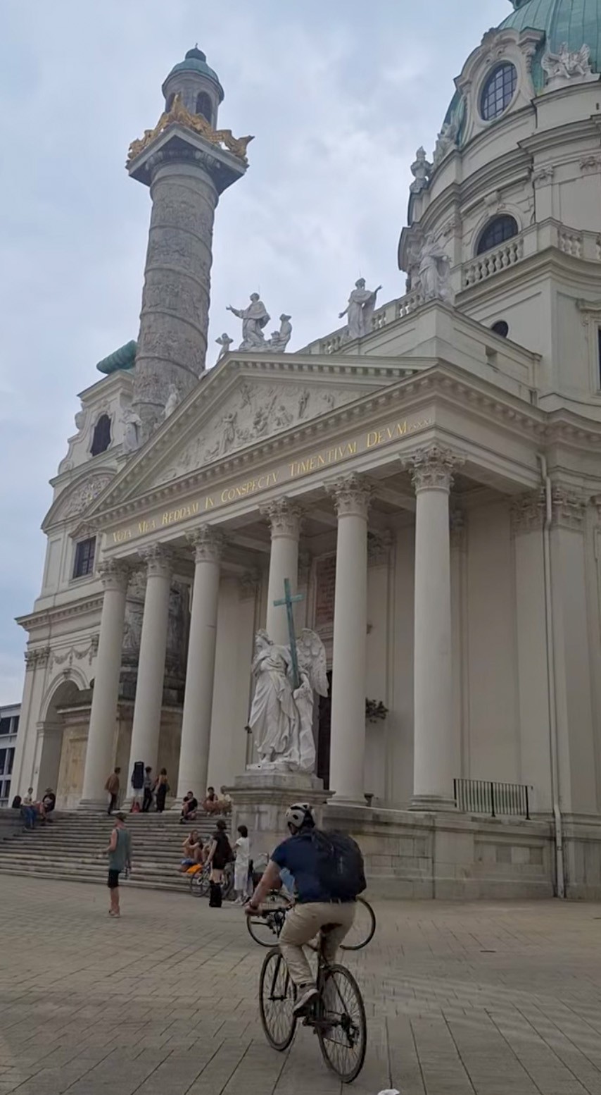 Karlskirche in Vienna — baroque dome, two twisted Trajan-style columns, sculptural pediment, cyclist rolling past on Karlsplatz