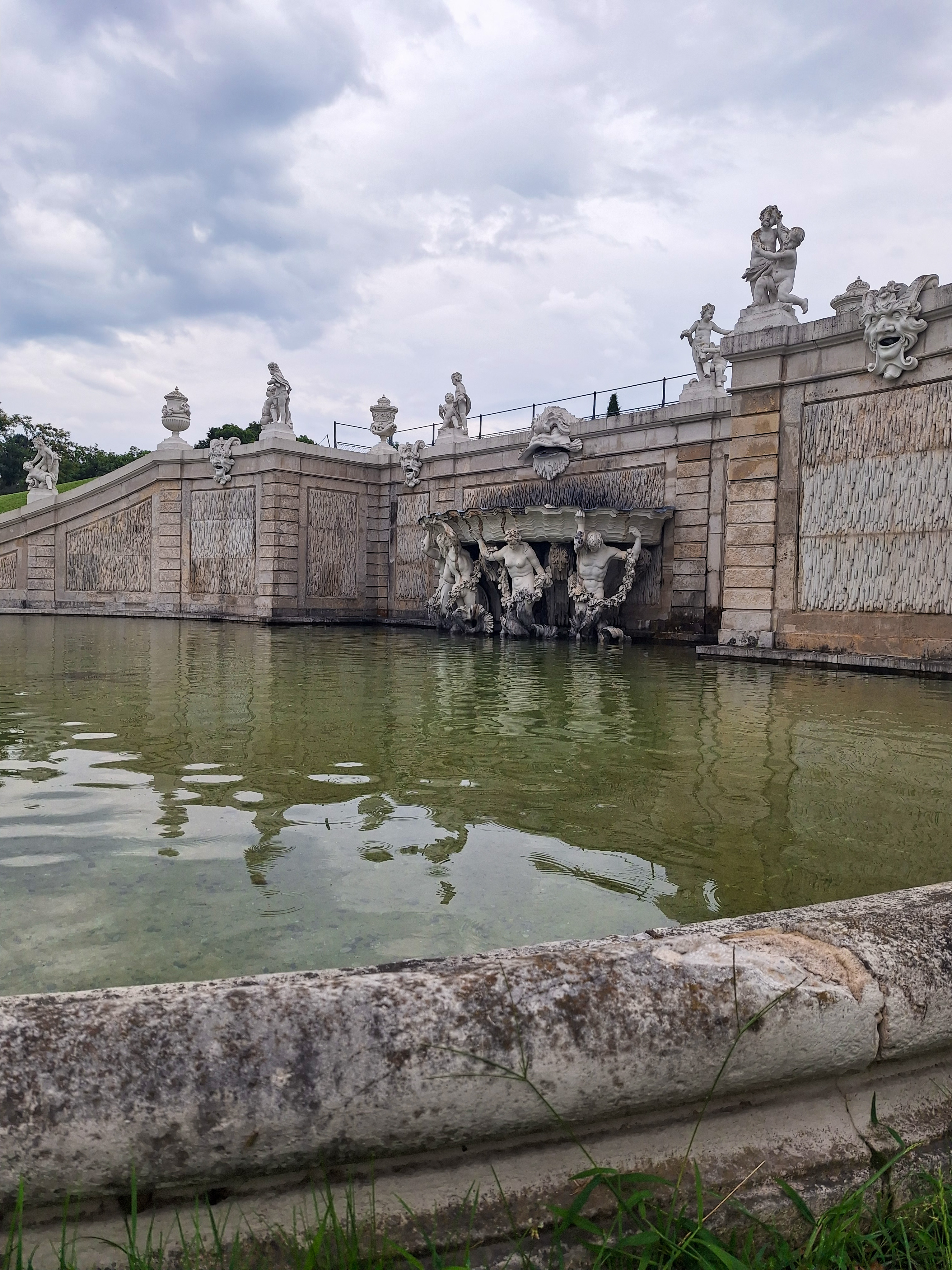 Baroque cascade at Schönbrunn — gods and nymphs on a marble wall with water running down, stormy summer sky above