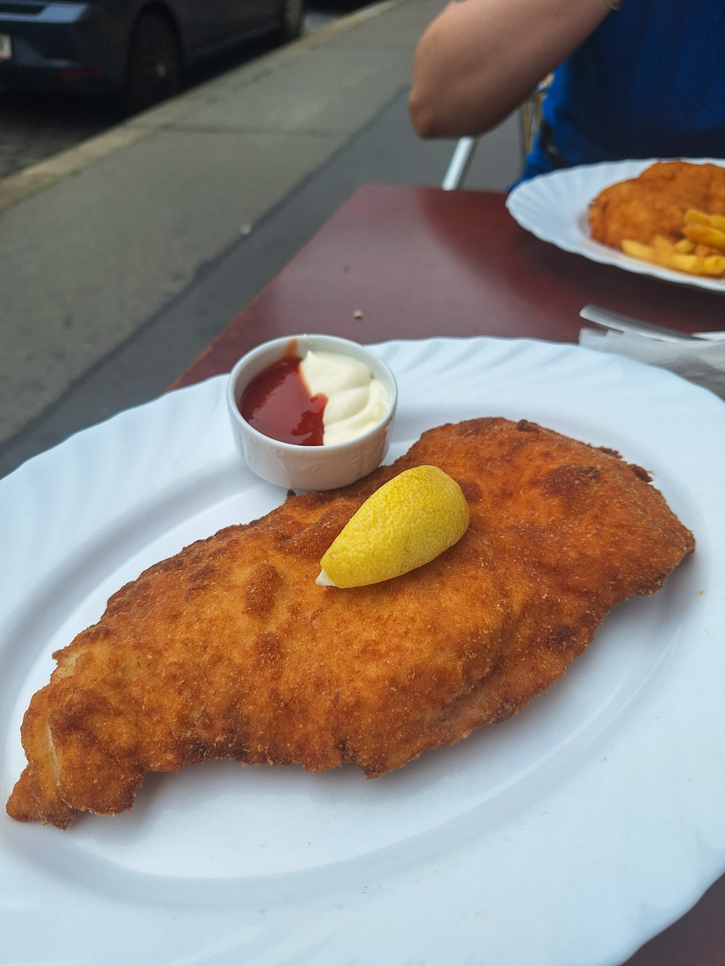 Classic Wiener Schnitzel with a wedge of lemon, on a white plate at a summer street table